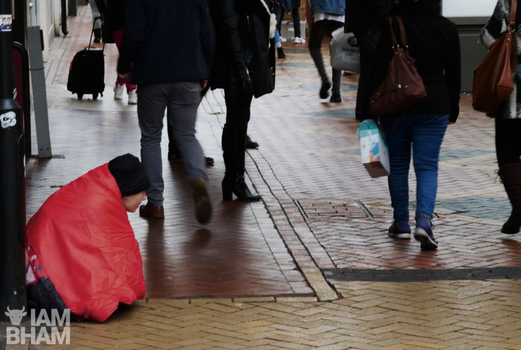 A man sits in New Street in Birmingham as shoppers past by 