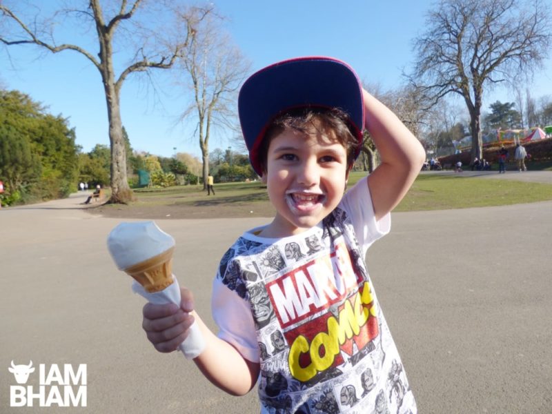 A young boy eats an ice-cream as he enjoys the sunshine in Cannon Hill Park in Birmingham