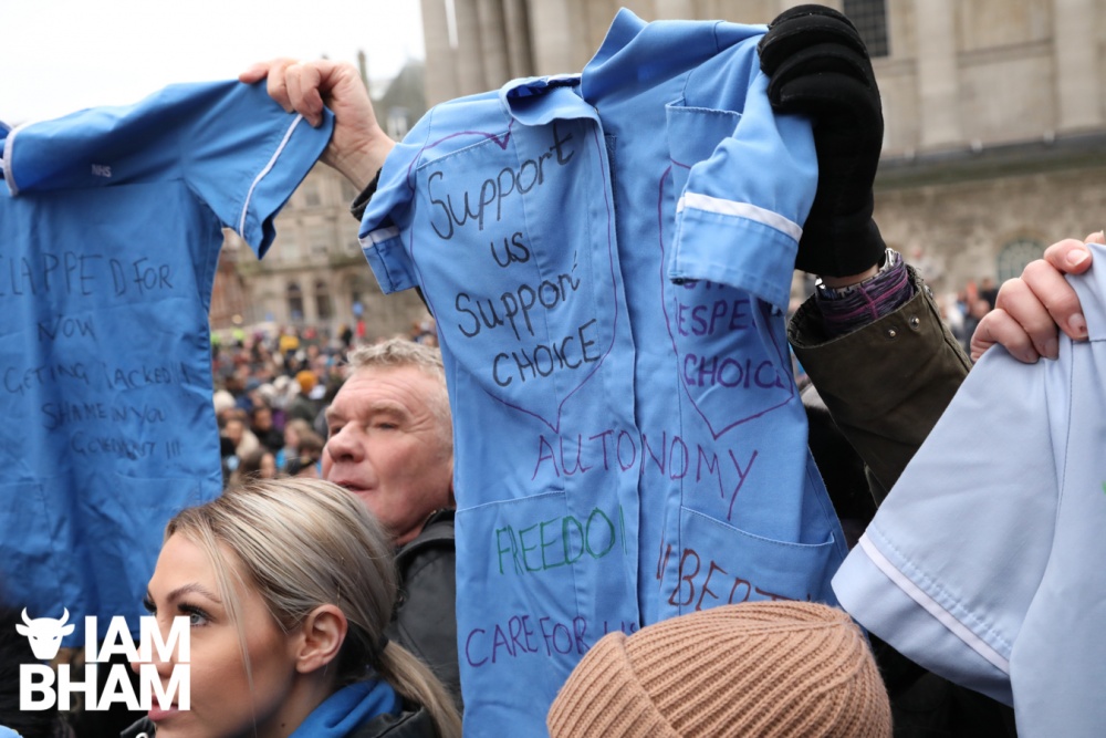 NHS uniforms adorned with messages are held up at the Birmingham mandated vaccinations protest