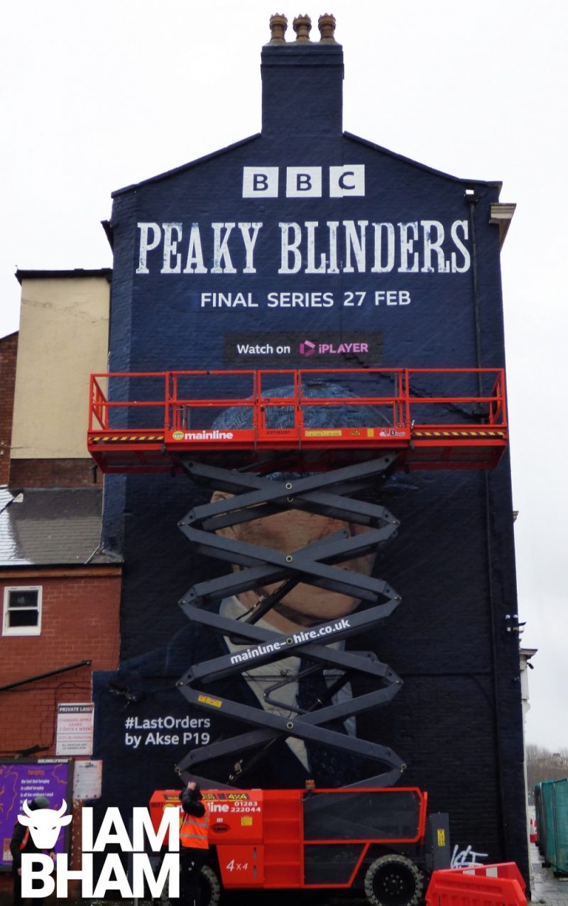A cherry picker is slowly lowered to unveil the gigantic Peaky Blinders mural in Digbeth Court car park 