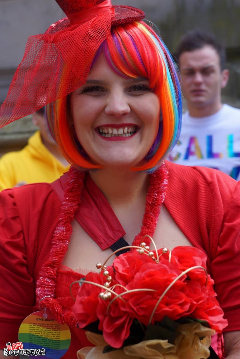 Smiling woman in full red dress and costume with rainbow hair at Birmingham Pride 2013 