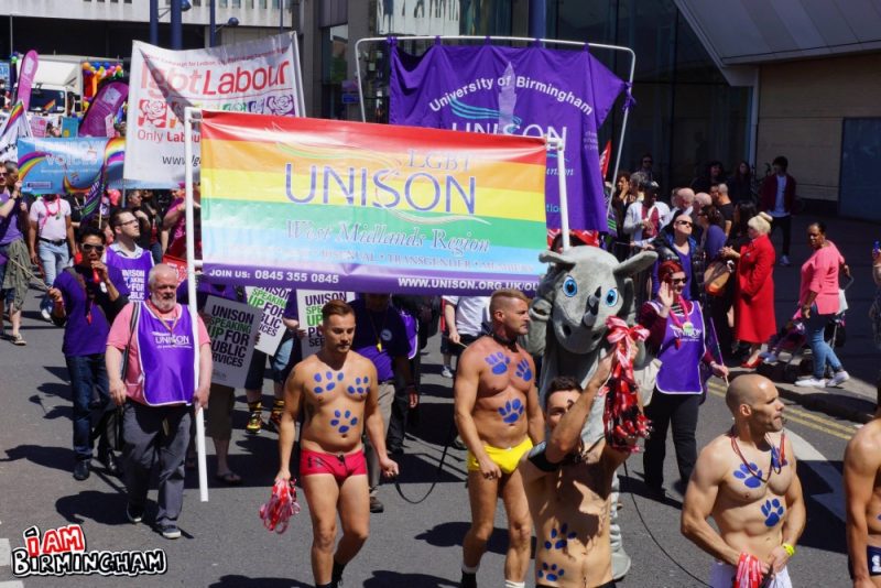 A rainbow Unison banner is carried by trade union members, with Prowler gay store muscle men walking ahead