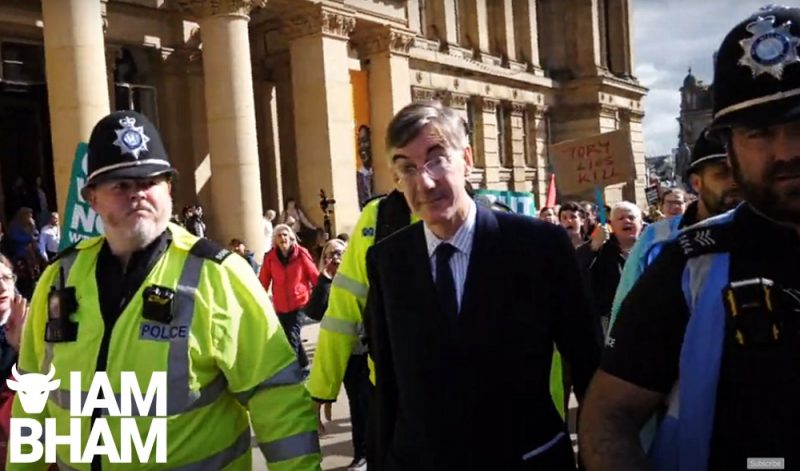 'Tory Lies Kill' banner held aloft by a protester as Jacob Rees-Mogg escorted by police
